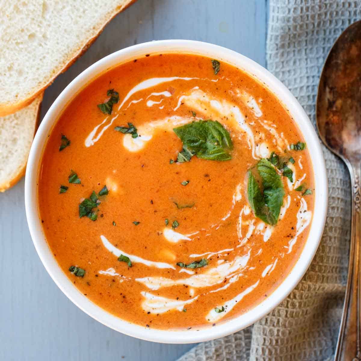 Tomato soup drizzled with heavy cream in a bowl with a spoon on the side.