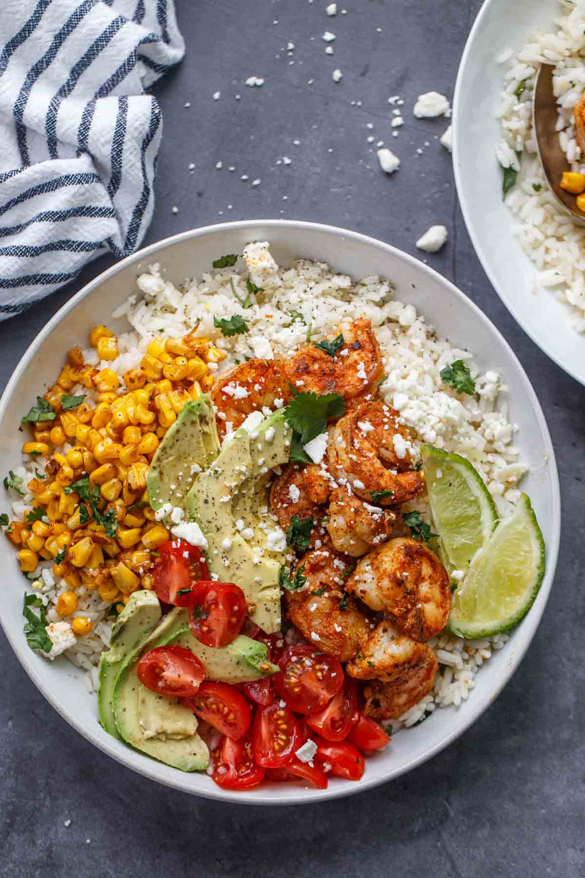 A serving bowl with rice, shrimp, avocado and corn with feta cheese.