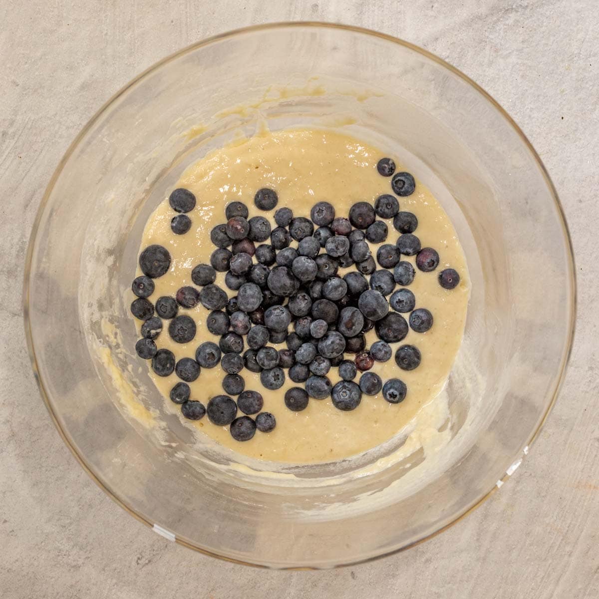 A mixing bowl containing a combination of dry and wet ingredients, with blueberries on top. 