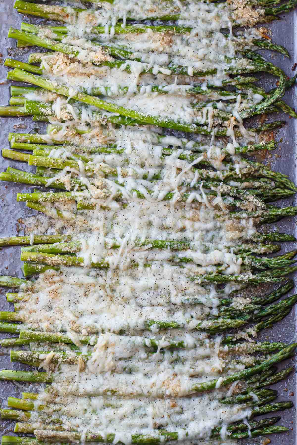 Baked asparagus in a baking sheet topped with cheese.