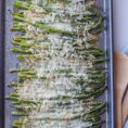 Cheesy asparagus in a bking sheet with a spoon on the side.