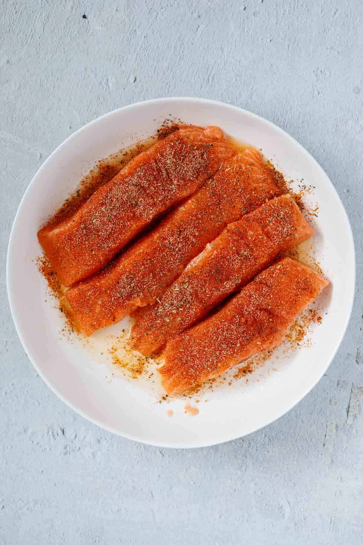 Salmon fillets arranged next to each other, coated in blackening seasoning. 