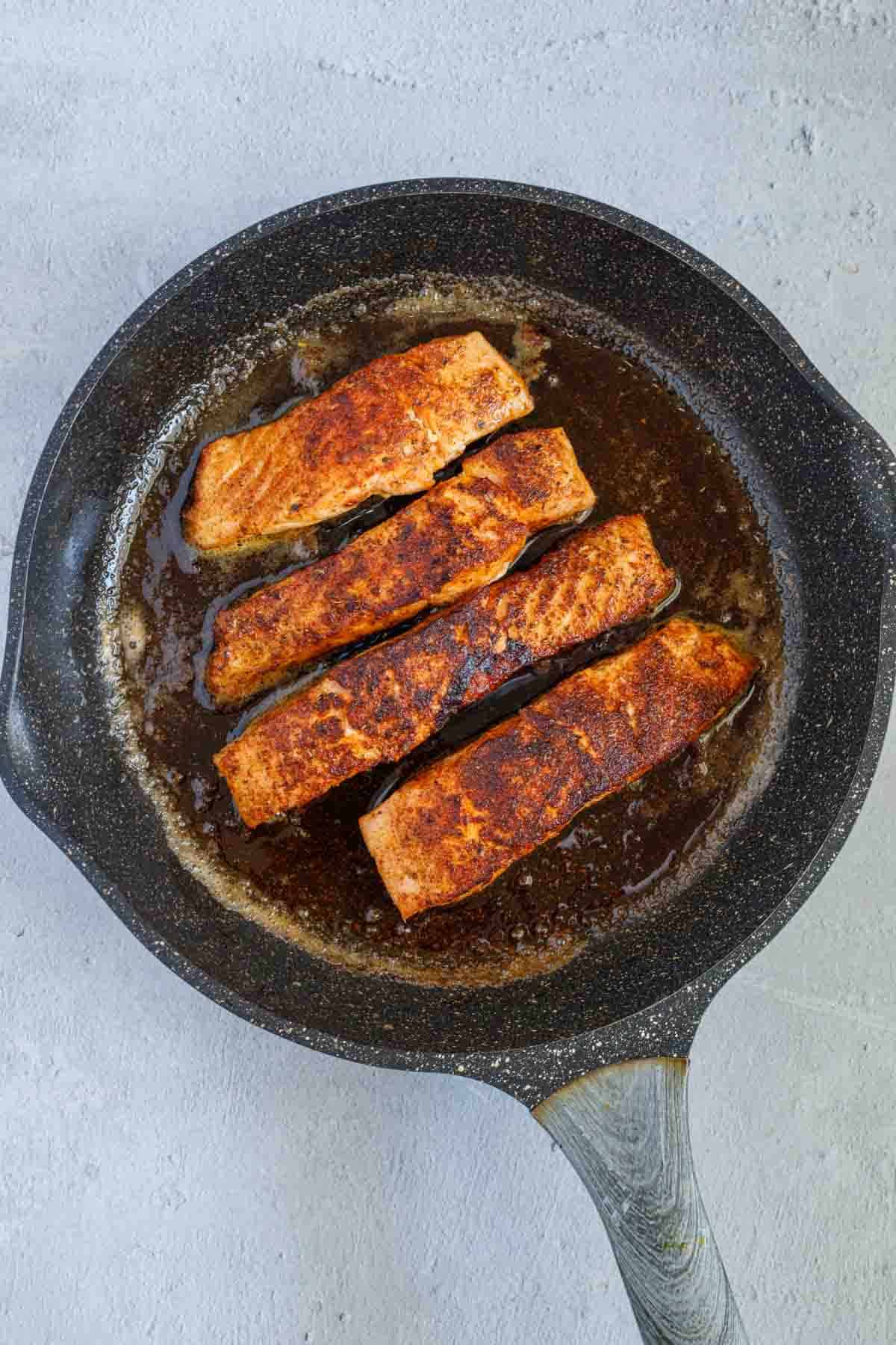 Salmon fillets cooking in a cast iron pan.