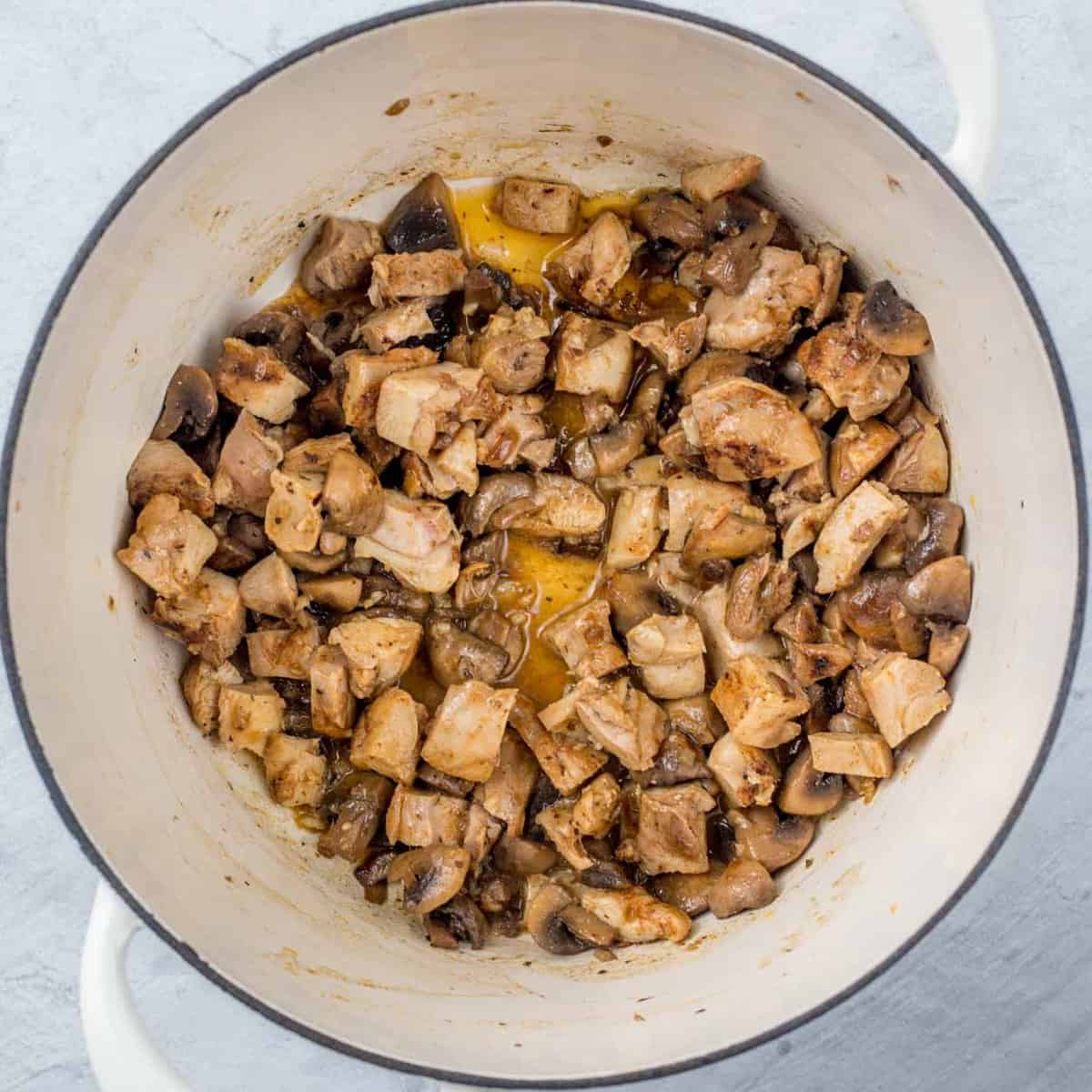 A pot with the cooking chicken and mushrooms.