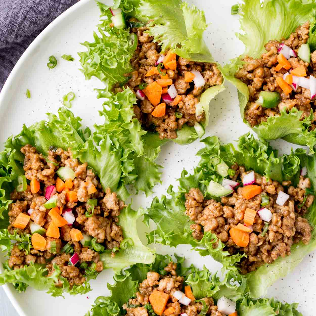 A plate of lettuce wraps, full of chicken, and garnished with toppings.