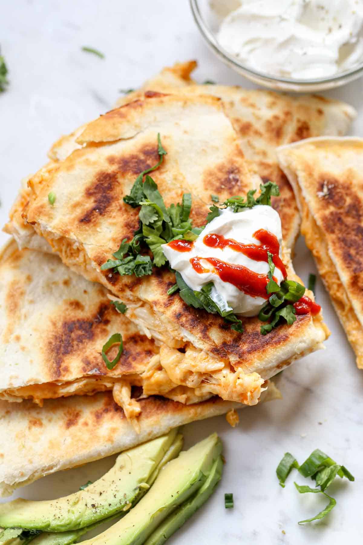 Slices of a chicken quesadilla with a dollop of sour cream on top, sprinkled with cilantro.
