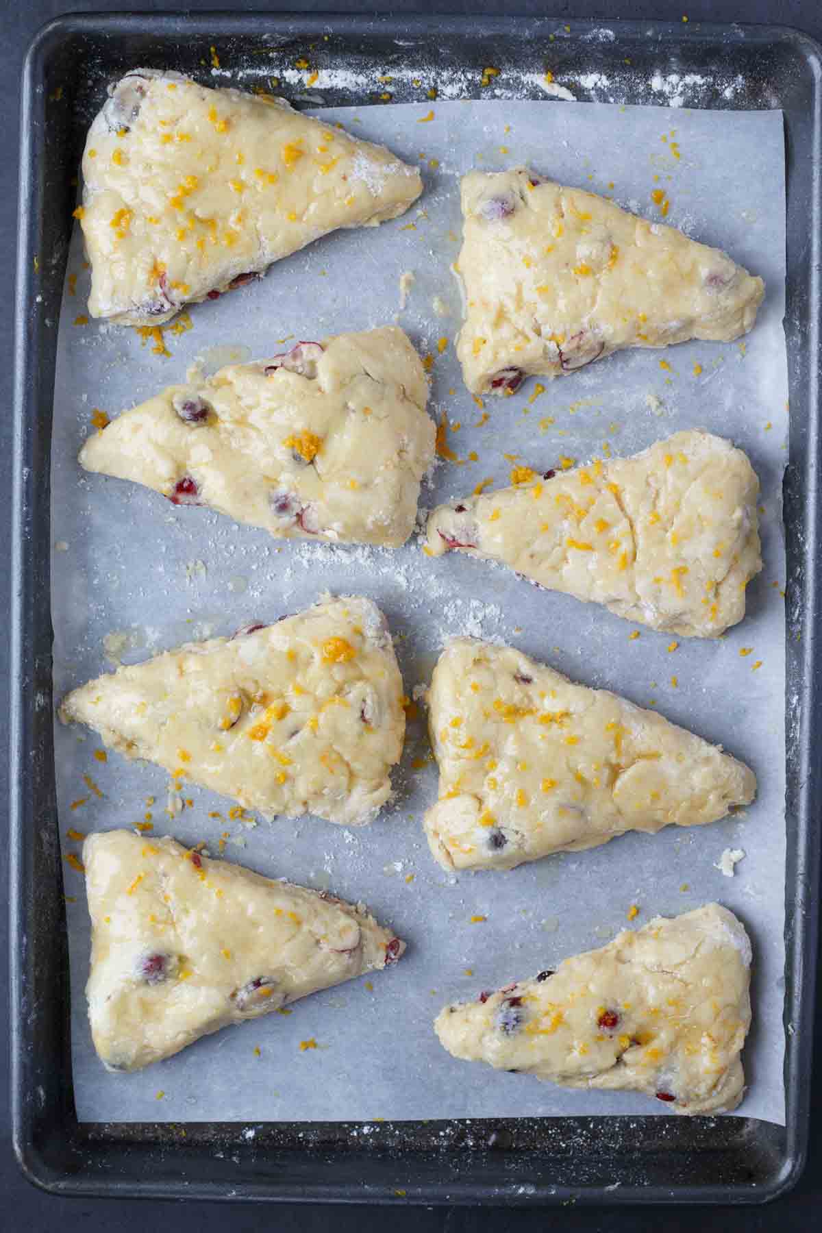 The scones are cut into triangle shaped, laid out on a baking pan with parchment paper. 