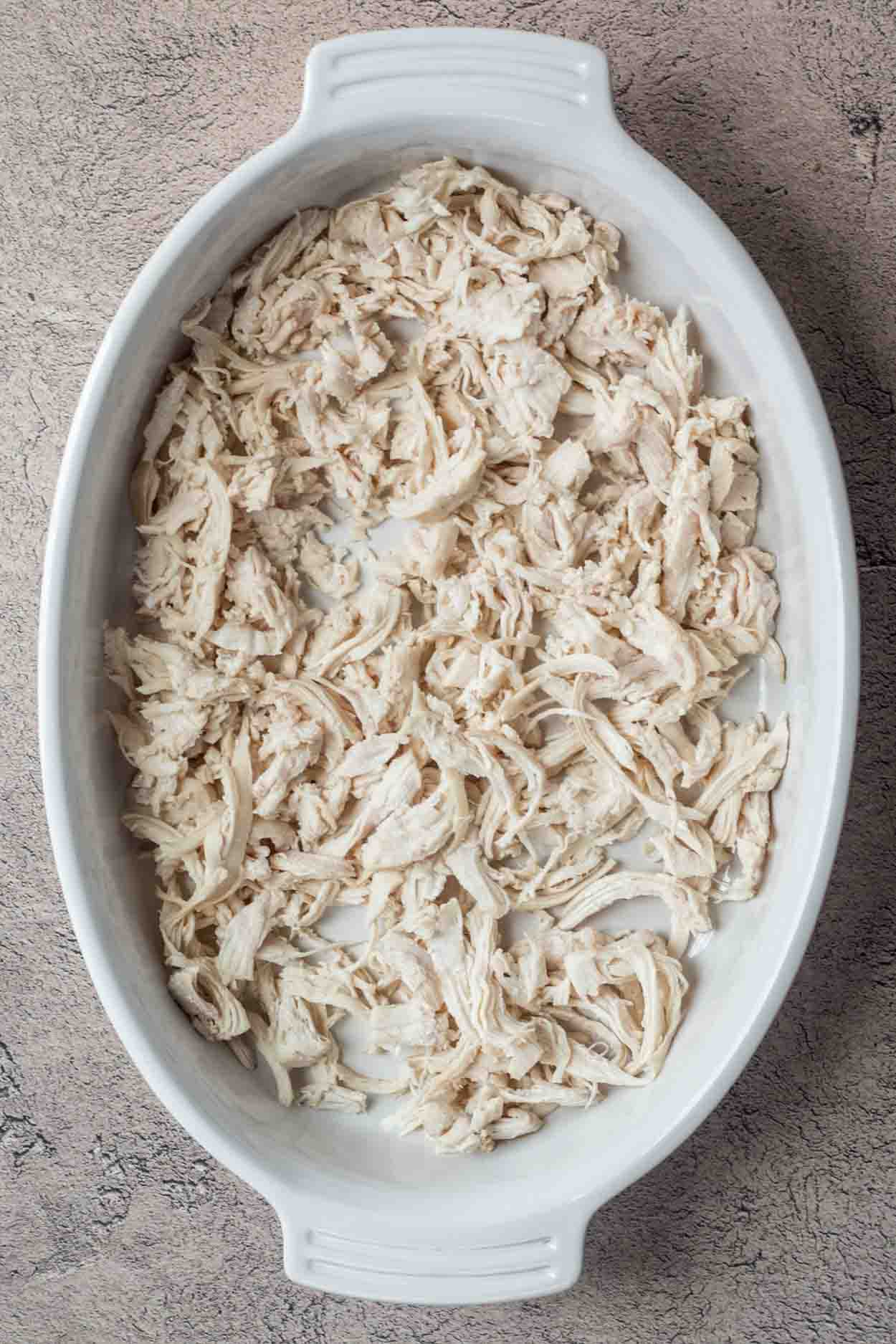 A casserole dish with shredded chicken evenly distributed.