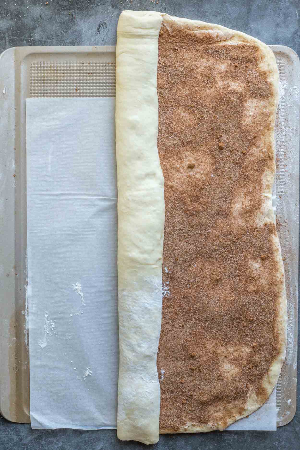 The cinnamon roll dough, rolled out into a large rectangle, with the cinnamon sugar mixture spread out.