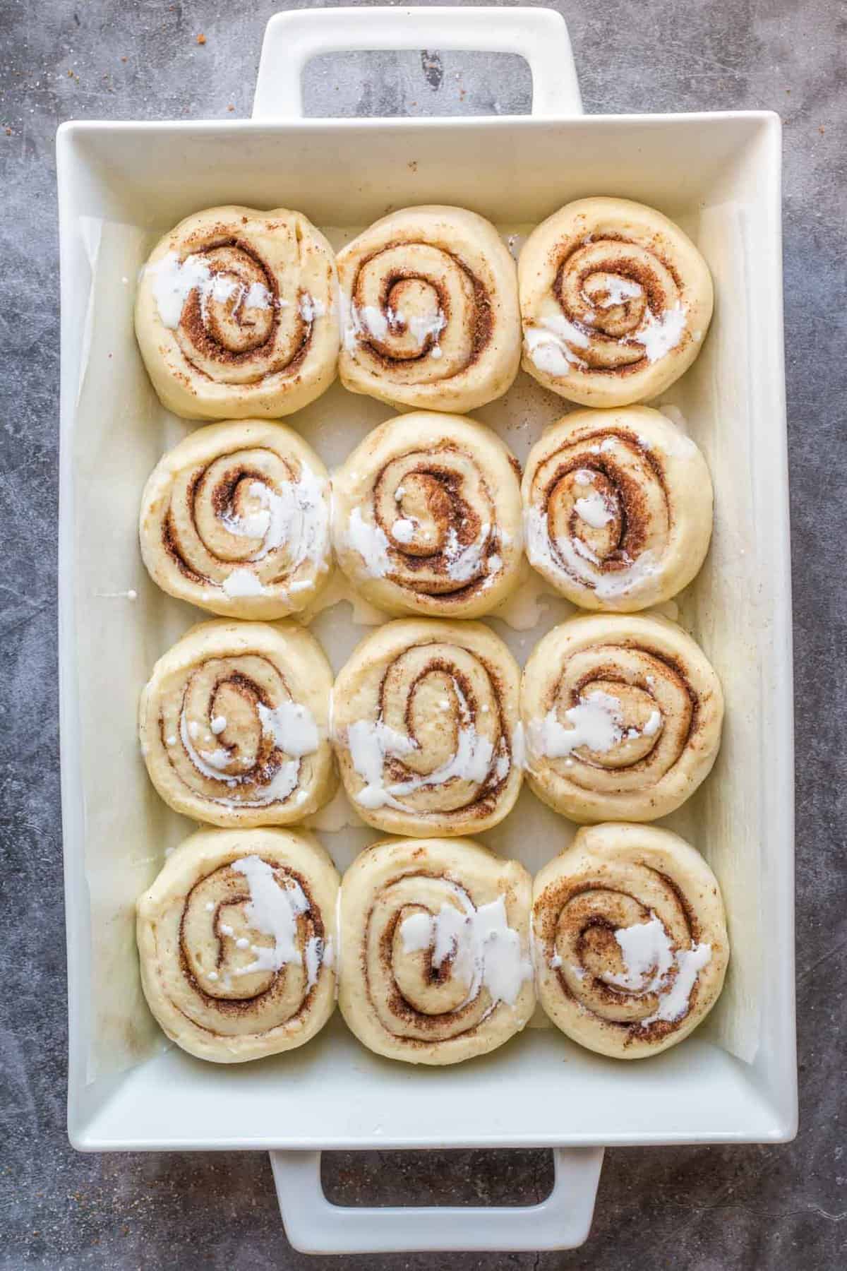 Cinnamon buns arranged in a baking dish, with heavy cream drizzled over them.