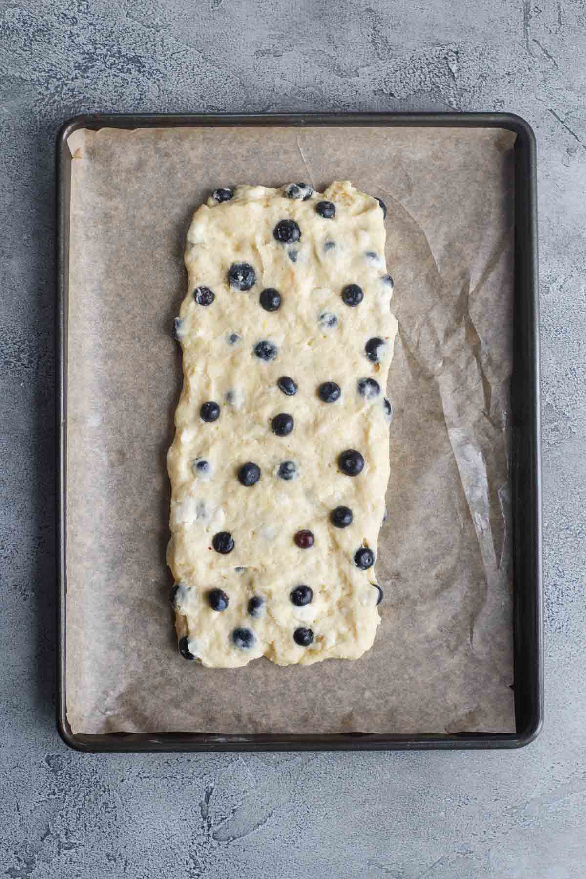 Blueberry scone dough formed into a rectangle on a baking sheet. 