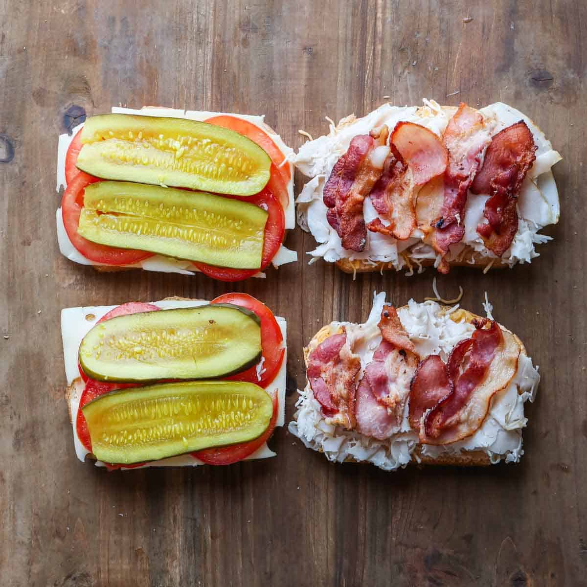 Four slices of bread, now topped with sliced tomatoes, sliced pickles, turkey and cooked bacon.