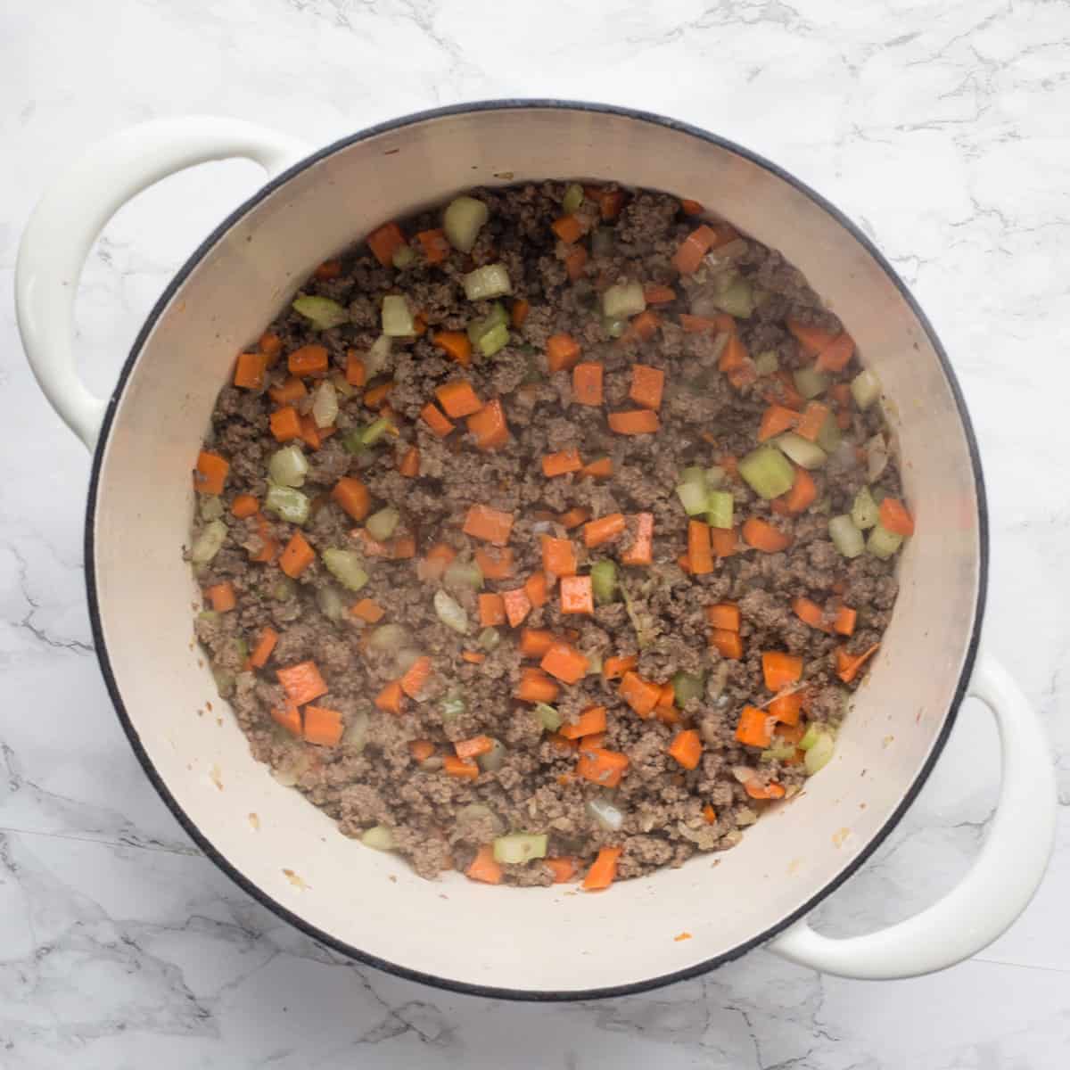 A pot with cooking ground beef with added carrots and celery.
