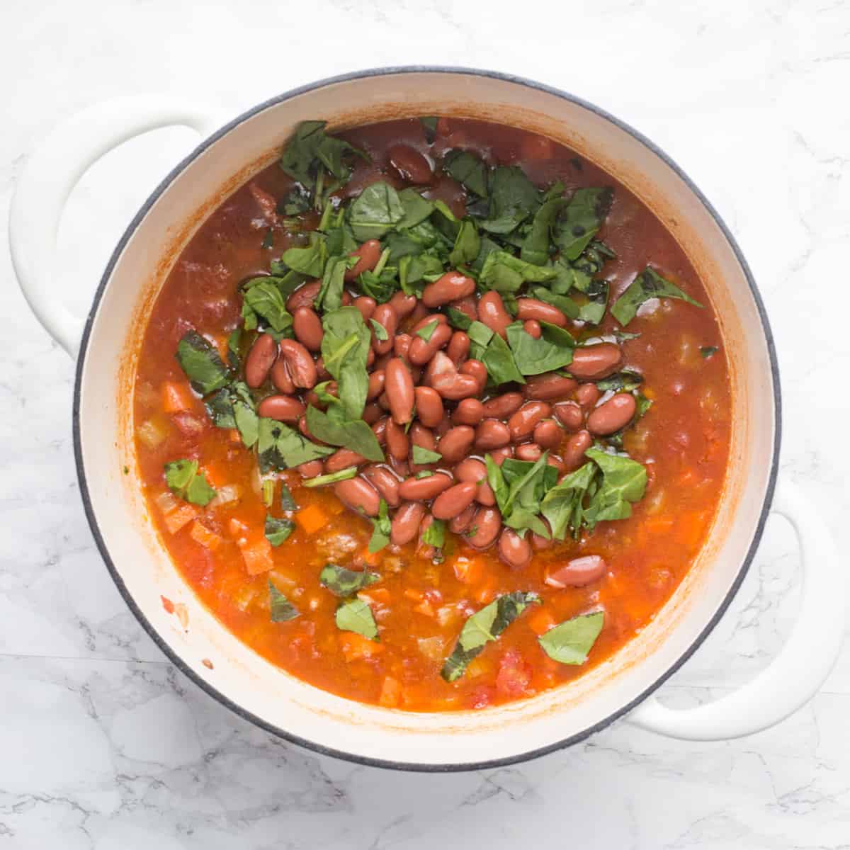 Spinach and beans are added to the pot of soup. 