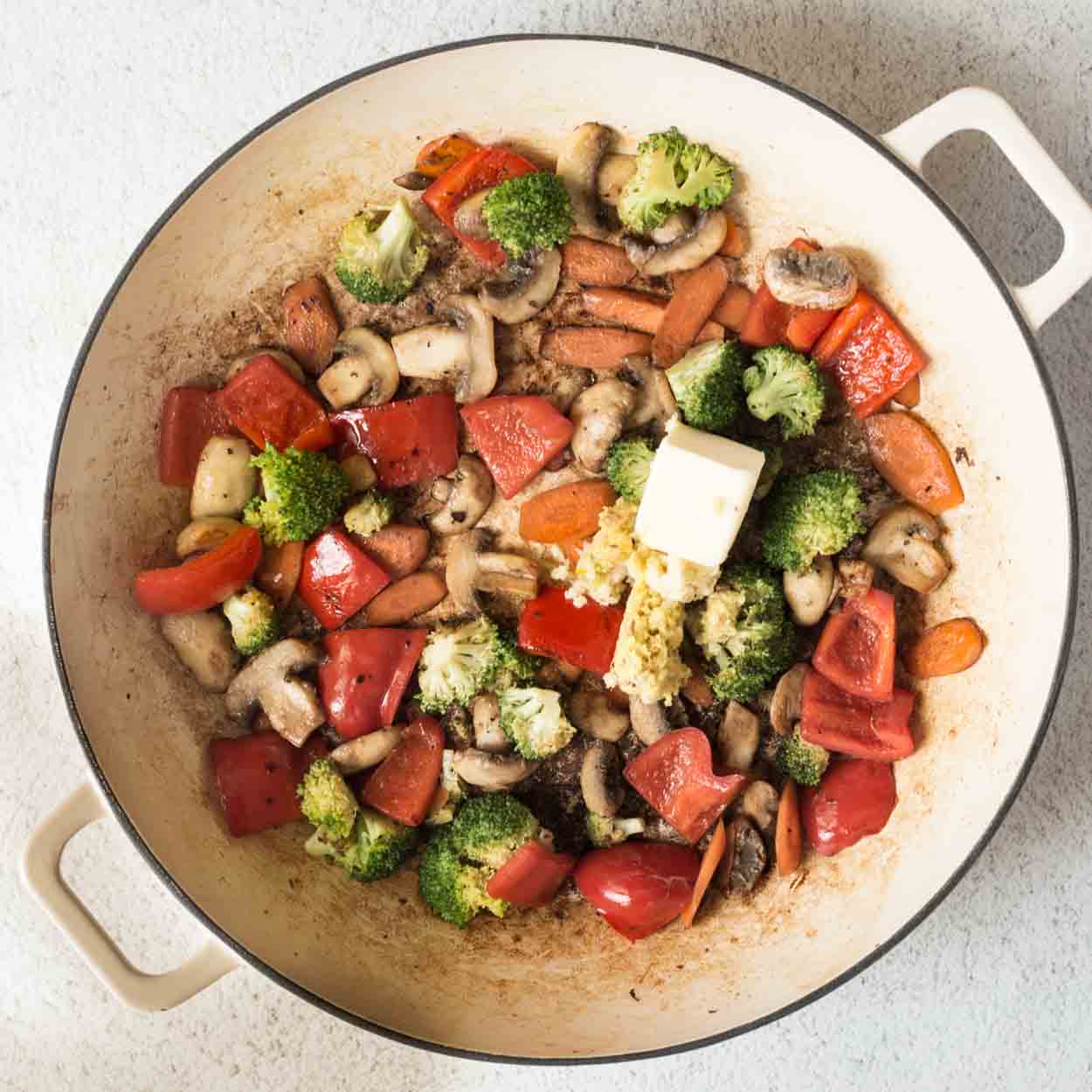 The skillet full of vegetables, with added butter. 