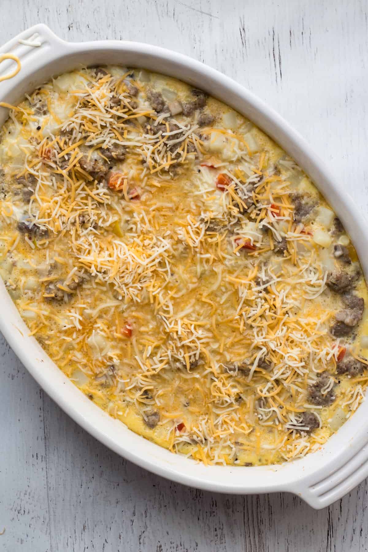 A casserole dish with the egg, vegetable mixture, topped with shredded cheese. 