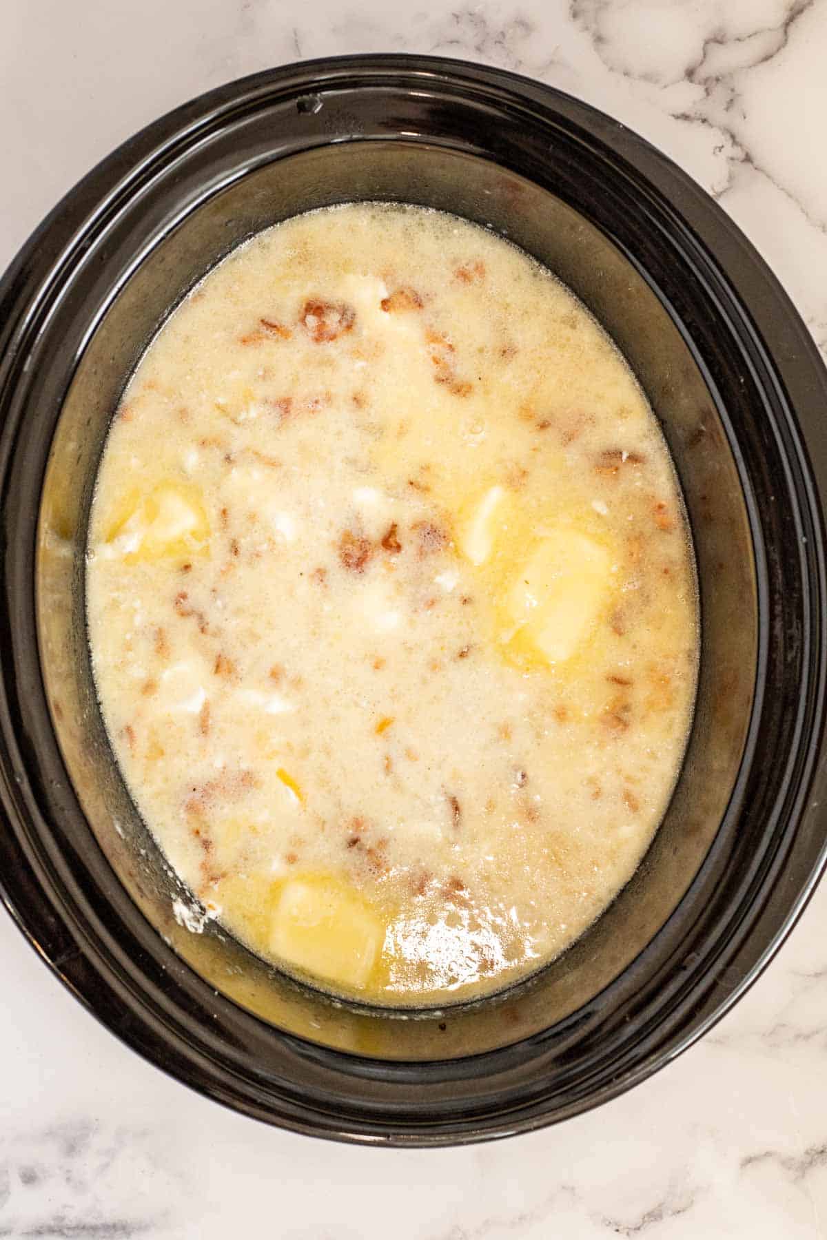 A black slow cooker containing the creamy potato soup after milk has been added.