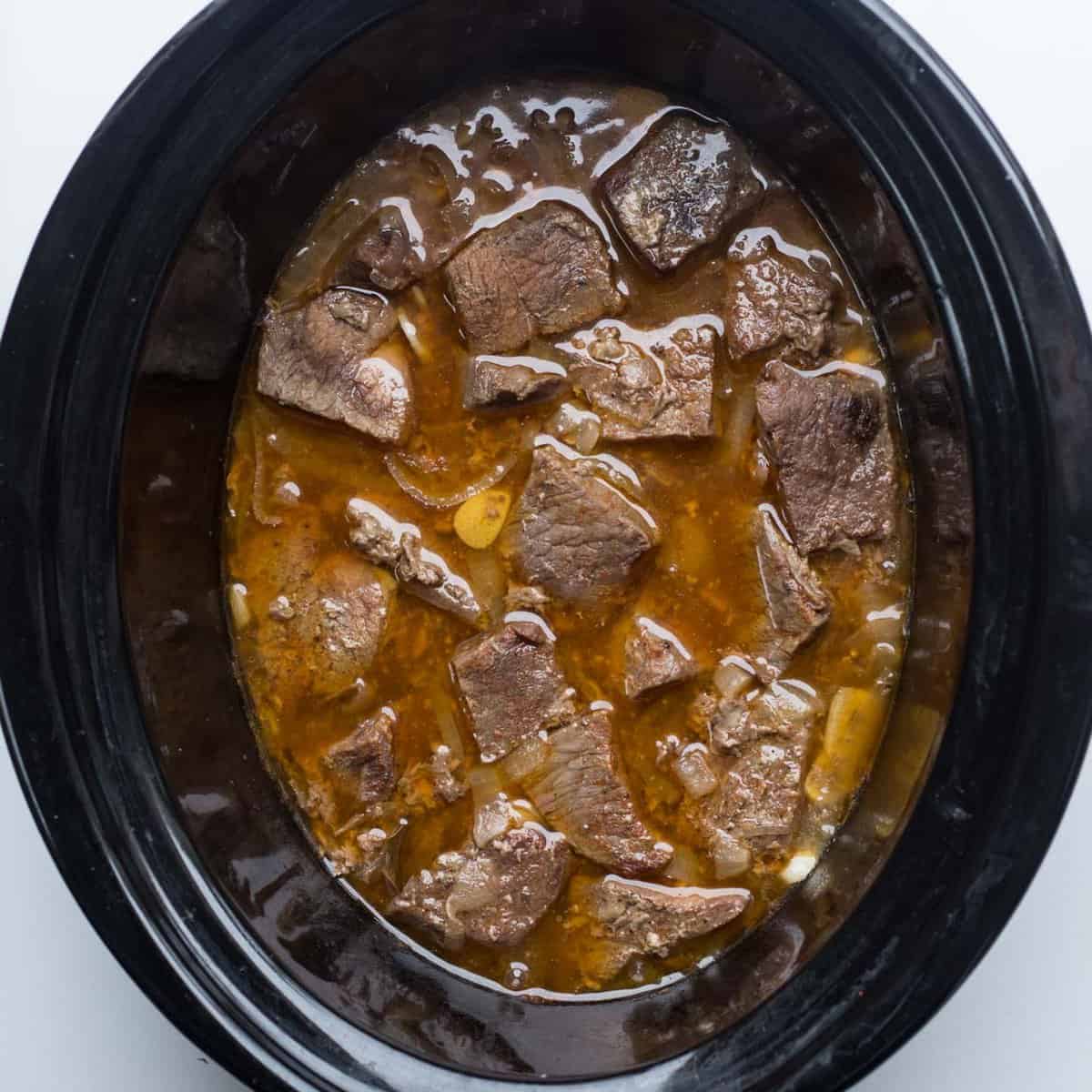 A crockpot with the cooking beef chunks. 