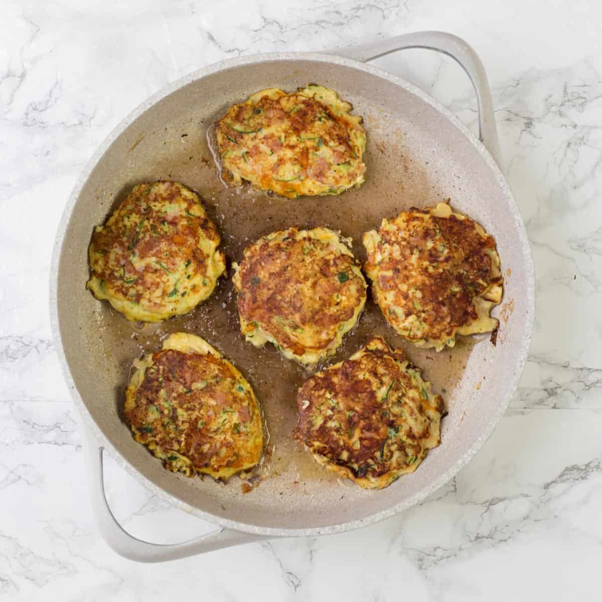 A pan with the flipped zucchini fritters. 