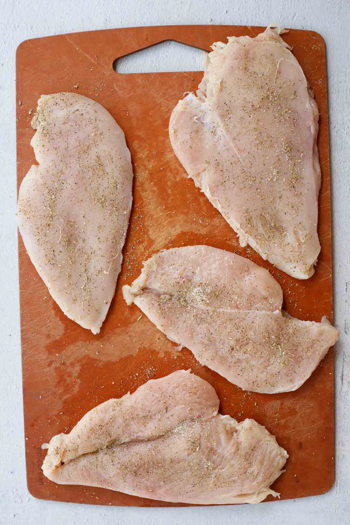 A cutting board with the raw chicken cutlets.
