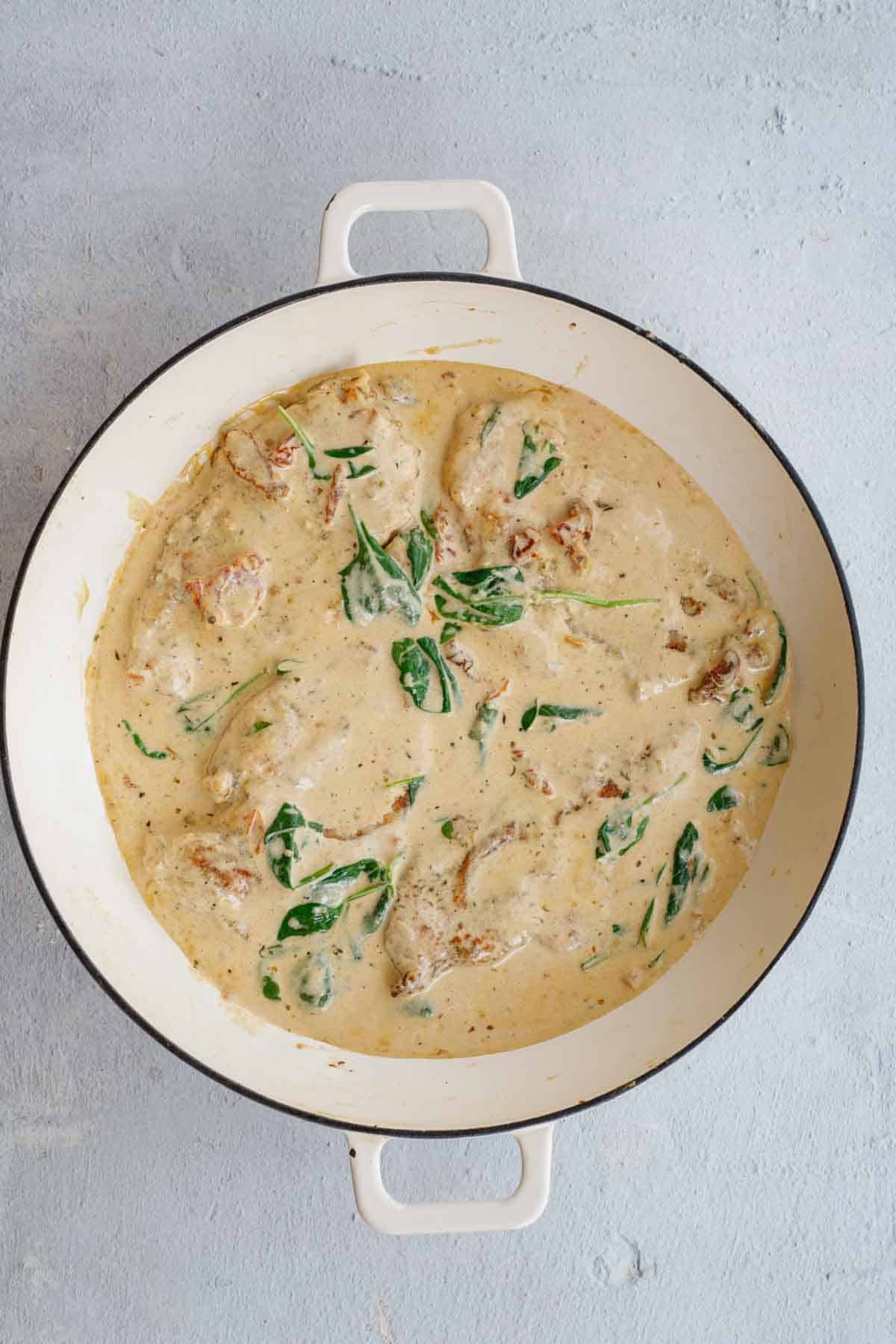 A pot of creamy tuscan chicken with added spinach.