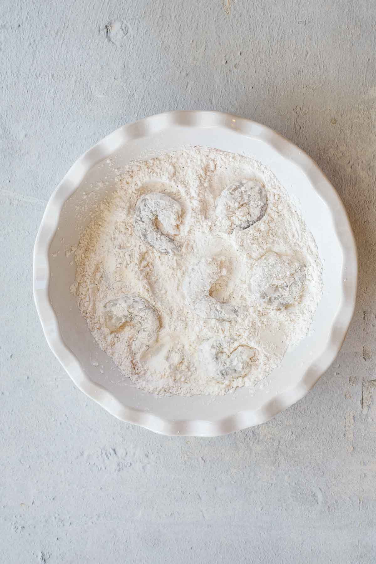 A white bowl with the shrimp in the flour mixture.