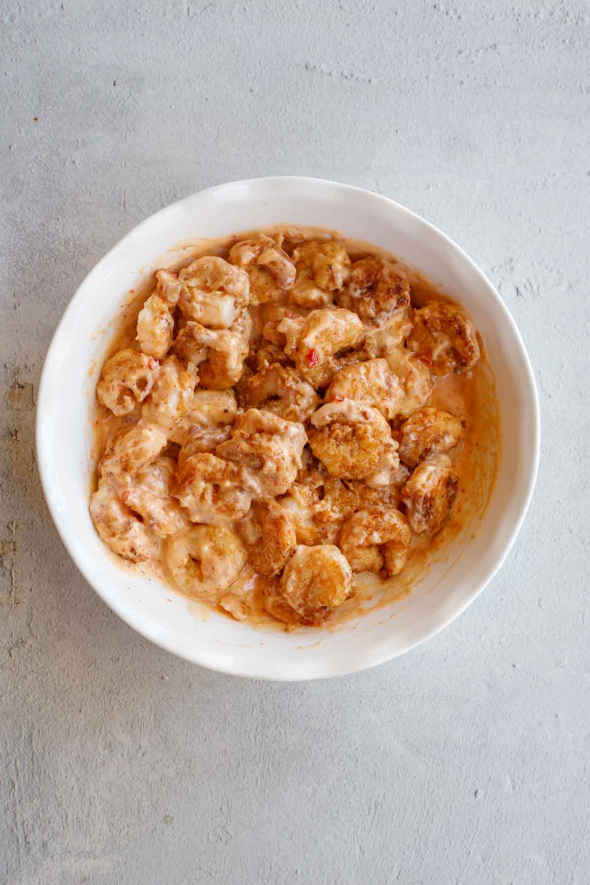 A white bowl with the shrimp being tossed in a sauce.