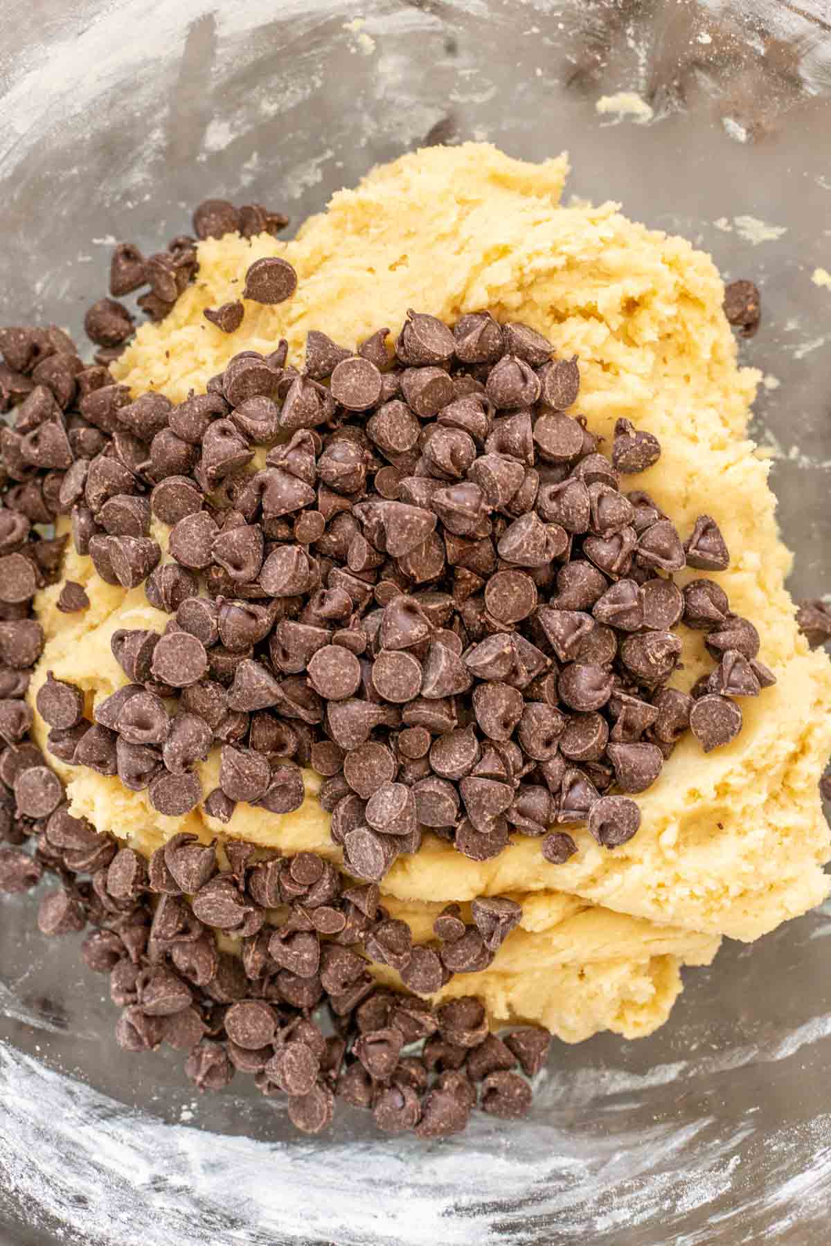 Chocolate chip cookie batter in a glass bowl, with chocolate chips. 