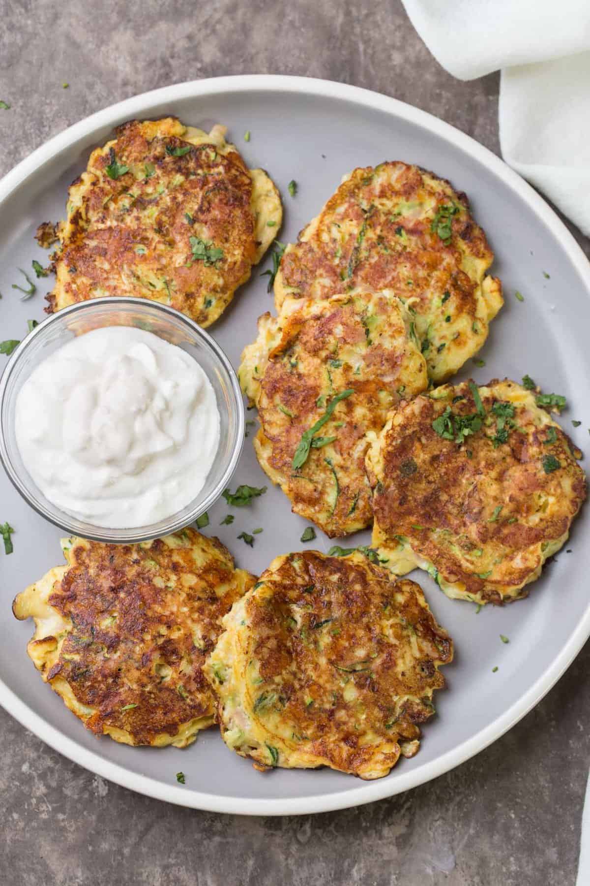 Breakfast Zucchini fritters on a plate with fresh herbs and sour cream dip.