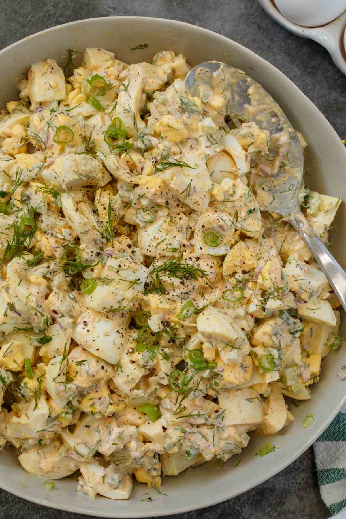 A gray bowl of egg salad with a silver spoon in it.