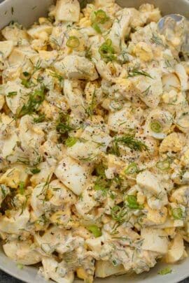 Egg salad mixed and topped with fresh greens and dill in a gray bowl.