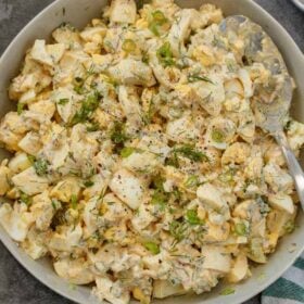 Egg salad mixed and topped with fresh greens and dill in a gray bowl.