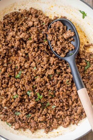 A pot of ground beef taco meat with a black spoon.