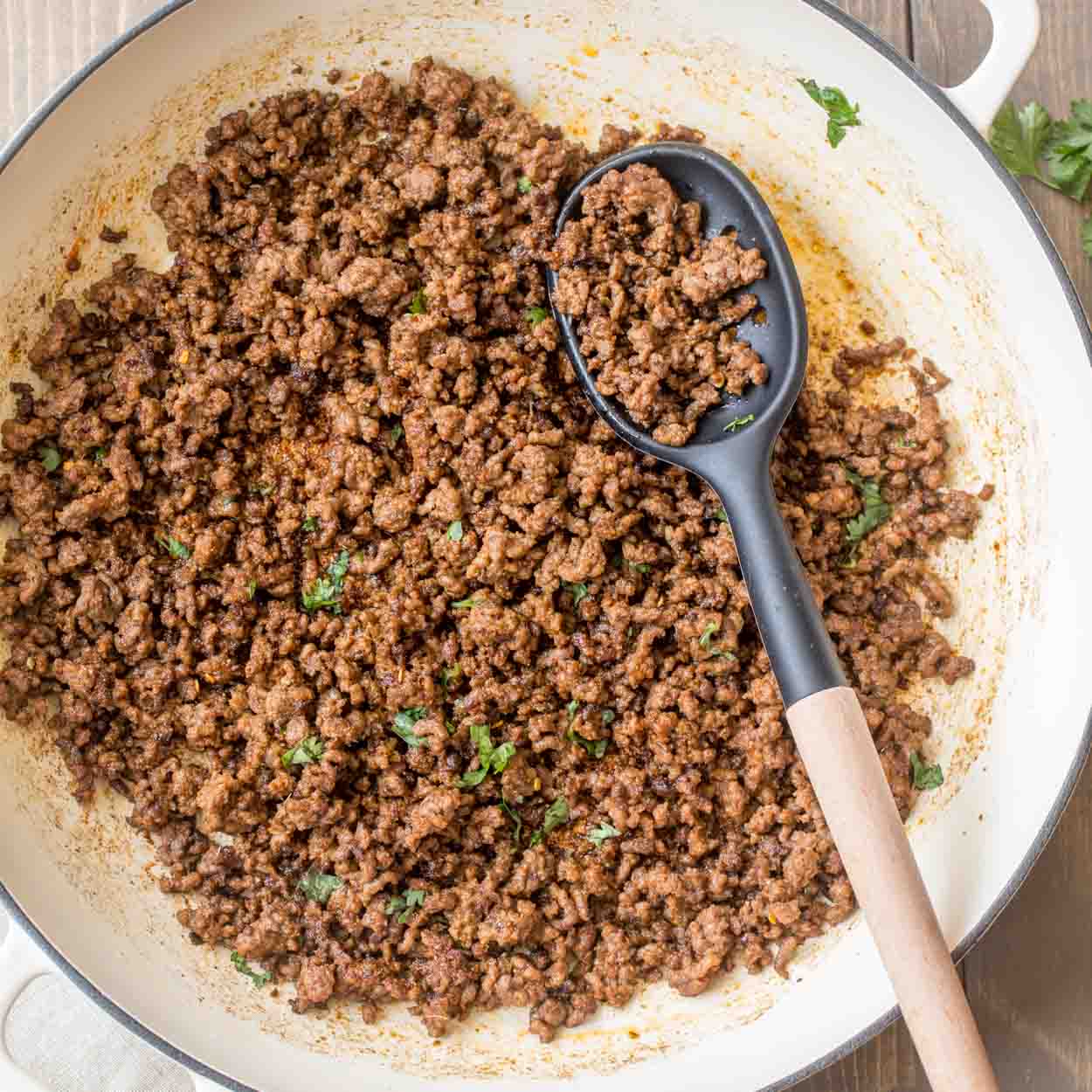 A pot of ground beef taco meat with a black spoon. 