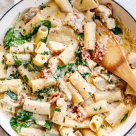 Tuscan chicken pasta in a pot with a wooden spoon.