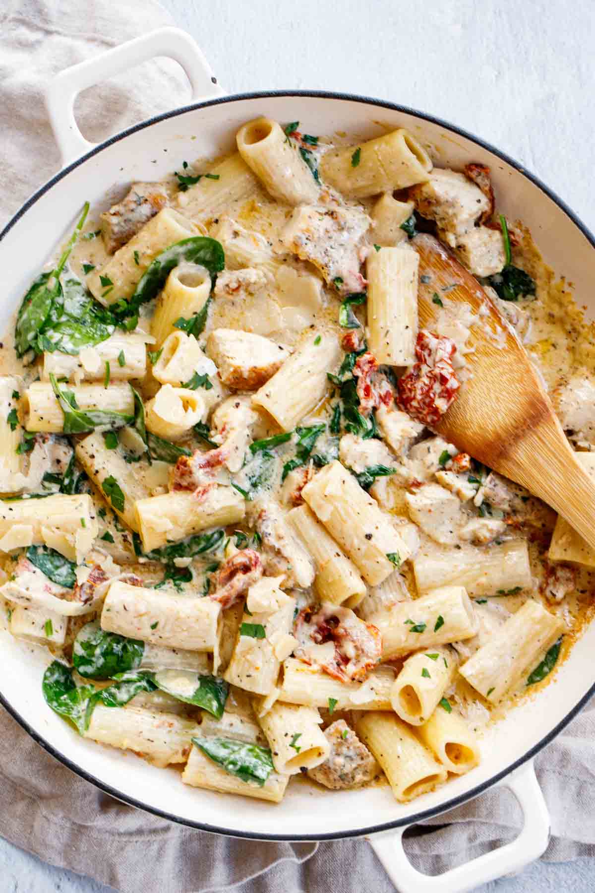 Tuscan chicken pasta in a pot with a wooden spoon. 