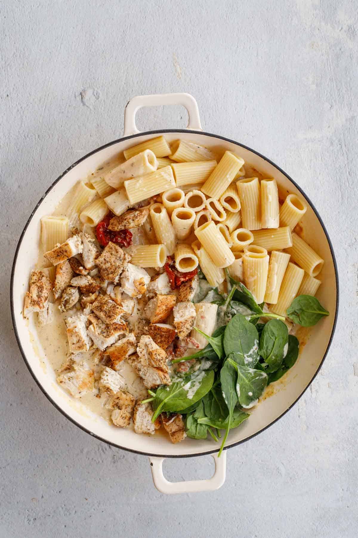 The pot with creamy tuscan sauce and the chicken, and pasta added to it.  
