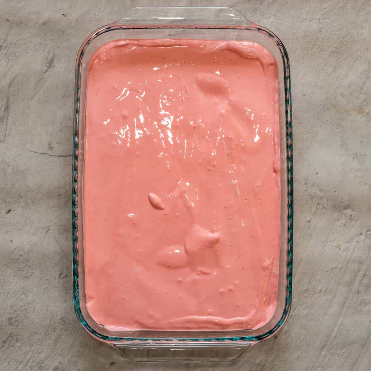 A baking dish with the pink creamy layer of jello on it.