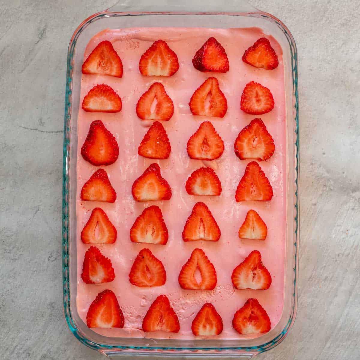 The baking dish with the creamy layer and sliced strawberries arranged on it. 