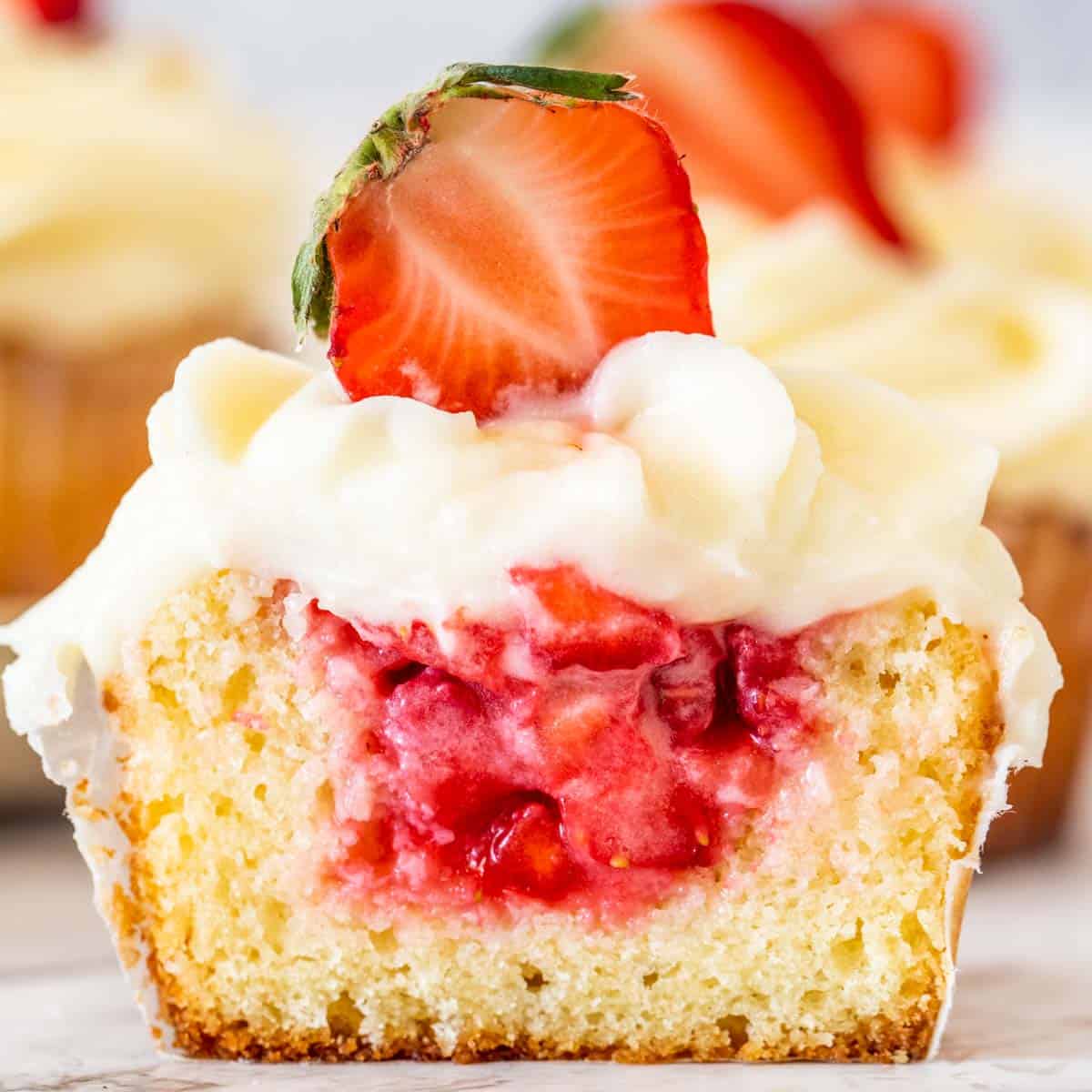 A strawberry shortcake cupcake sliced in half to show the strawberry filling inside of the cupcake. 