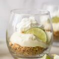 A glass cup with the layered key lime pie, garnished with a sliced lemon.