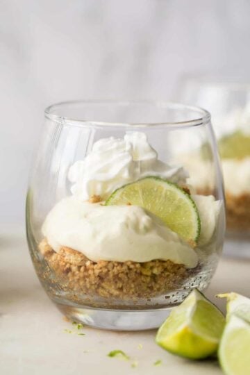 A glass cup with the layered key lime pie, garnished with a sliced lemon.