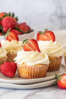 Three strawberry shortcake cupcakes, topped with a sliced strawberry.