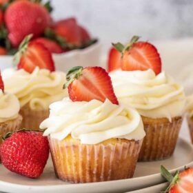 Three strawberry shortcake cupcakes, topped with a sliced strawberry.