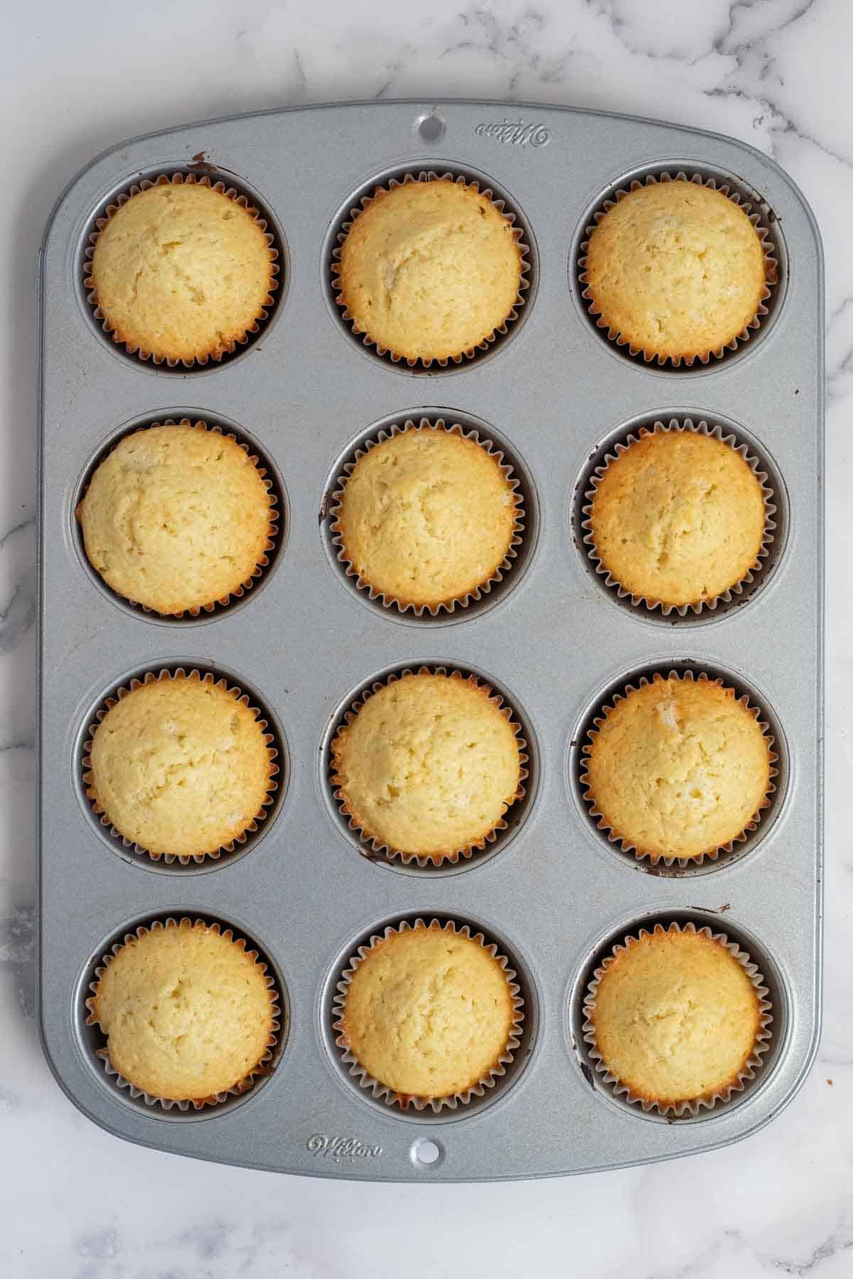 A muffin pan with baking vanilla cupcakes.