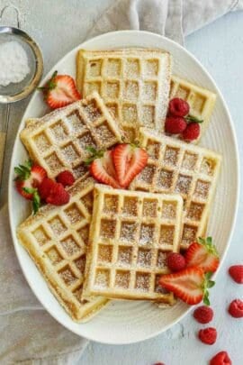 A white plate with the Belgian waffles on top arranged with sliced strawberries.