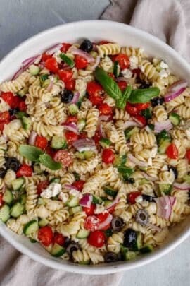 A white bowl of greek pasta salad.