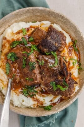 A plate with creamy mashed potatoes topped with juicy short ribs.