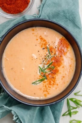A bowl with spicy mayo topped with seasoning and green onion.