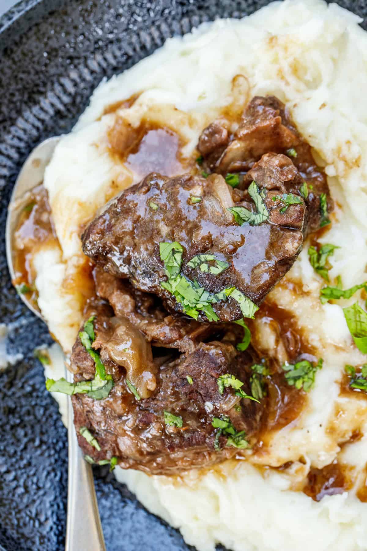 Our slow cooker short ribs are tender, fall off the bone protein. The short ribs are slow cooked in red wine broth and makes for the most flavorful dish. A plate with creamy mashed potatoes, topped with slow cooker short ribs.